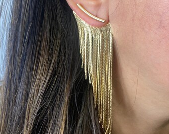May include: Gold dangle earrings with a thin bar that goes through the earlobe and a long chain of gold strands hanging down.