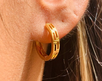 May include: Gold hoop earrings with a geometric design. The earrings are made of a thick, solid metal and have a polished finish.