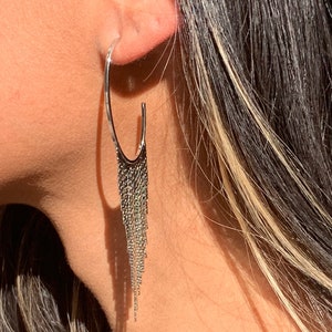 May include: Silver hoop earrings with a long chain fringe dangling from the bottom.