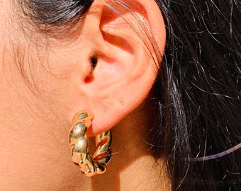 May include: Gold hoop earrings with a twisted design. The earrings are thick and chunky.