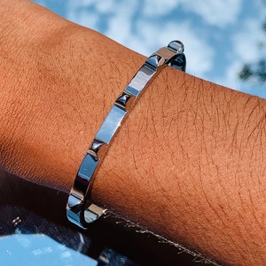 May include: A silver bracelet with a row of small, pointed studs. The bracelet is on a person's wrist.