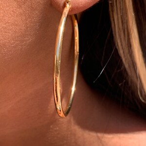 May include: Gold hoop earrings with a smooth, polished finish. The earrings are large and circular, with a diameter of approximately 2 inches.