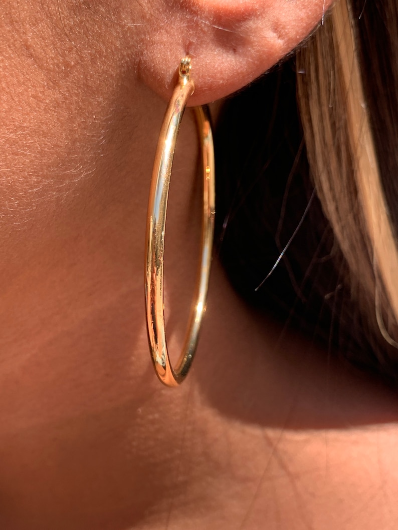 May include: Gold hoop earrings with a smooth, polished finish. The earrings are large and circular, with a diameter of approximately 2 inches.