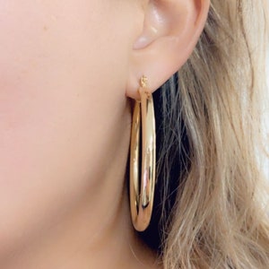 May include: Gold hoop earrings with a smooth, shiny finish. The earrings are large and circular, with a diameter of approximately 2 inches.