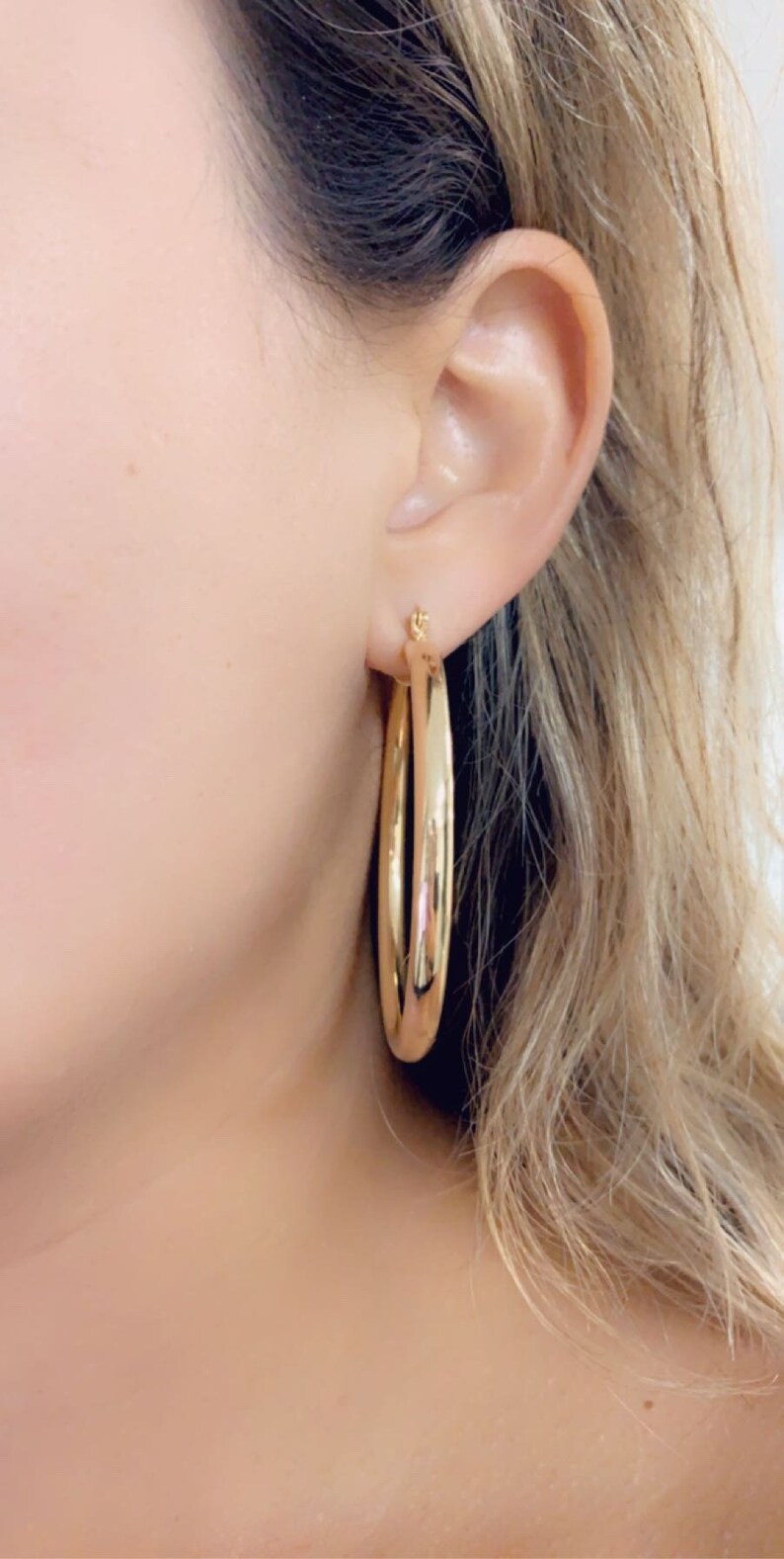 May include: Gold hoop earrings with a smooth, shiny finish. The earrings are large and circular, with a diameter of approximately 2 inches.