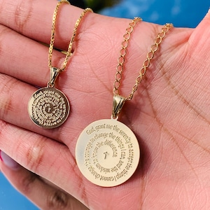 May include: Two gold necklaces with circular pendants. The larger pendant has the Serenity Prayer engraved on it. The smaller pendant has a circular design with a cross in the center.