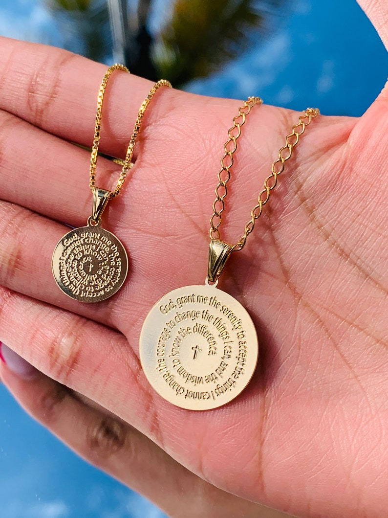 May include: Two gold necklaces with circular pendants. The larger pendant has the Serenity Prayer engraved on it. The smaller pendant has a circular design with a cross in the center.