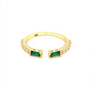 May include: Gold ring with a split band design, featuring two emerald green stones and a row of clear cubic zirconia stones.