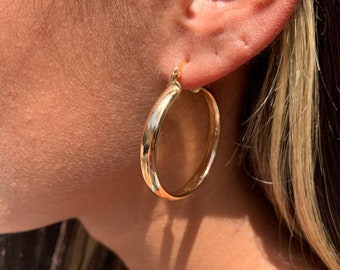 May include: Gold hoop earrings with a smooth, polished finish. The earrings are large and circular, with a diameter of approximately 2 inches.