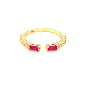 May include: A gold ring with two red gemstones and a row of clear gemstones. The ring is open on the sides.