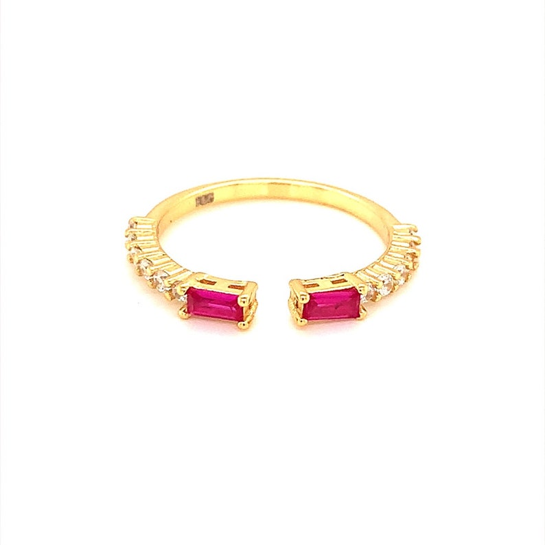 May include: A gold ring with two red gemstones and a row of clear gemstones. The ring is open on the sides.