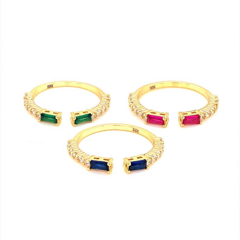 May include: Three gold rings with a split band design. Each ring has a row of small clear stones and a larger colored stone in the center. The stones are green, red, and blue.