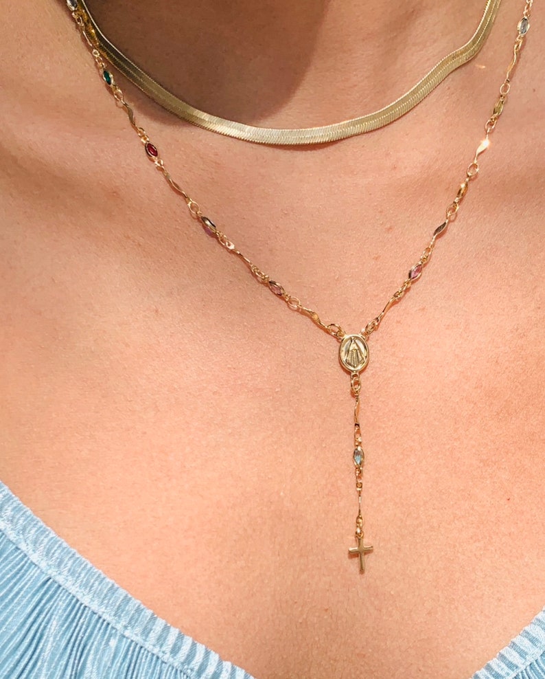 May include: A gold chain necklace with a small cross charm and a pendant featuring the Virgin Mary. The necklace has small colorful beads.