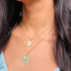 May include: A gold chain necklace with two round pendants. The pendants are engraved with intricate designs.