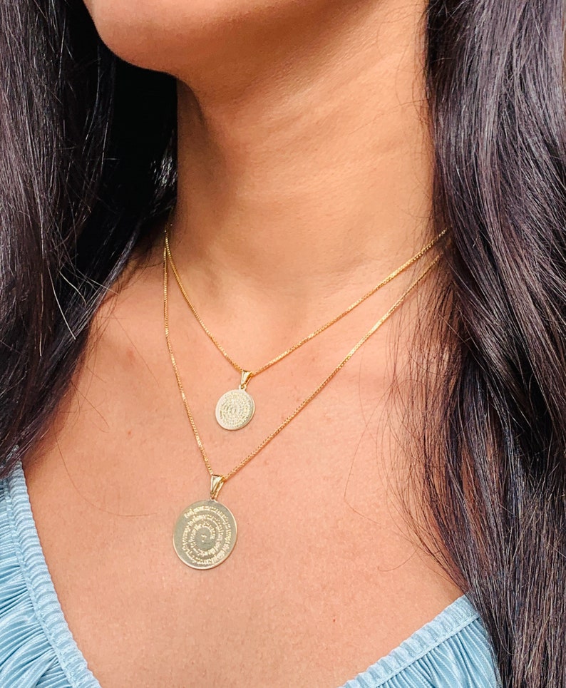 May include: A gold chain necklace with two round pendants. The pendants are engraved with intricate designs.