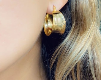 May include: Gold hoop earrings with a textured, wavy design. The earrings are a classic style and would be a great addition to any jewelry collection.