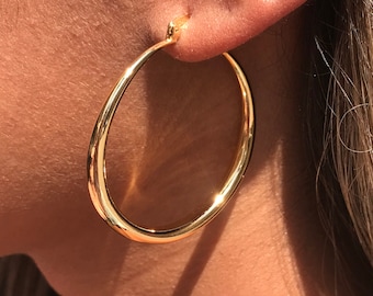 May include: Gold hoop earrings. The earrings are large and circular, with a smooth, polished finish.
