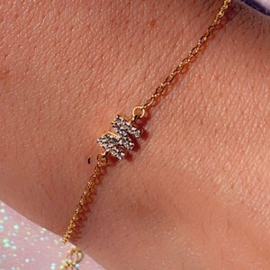 Könnte beinhalten: Ein goldenes Kettenarmband mit einem kleinen, glitzernden Buchstaben "M" Anhänger.
