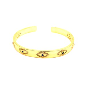 May include: Gold bangle bracelet with a repeating pattern of blue evil eye charms. The charms are set with small clear stones.