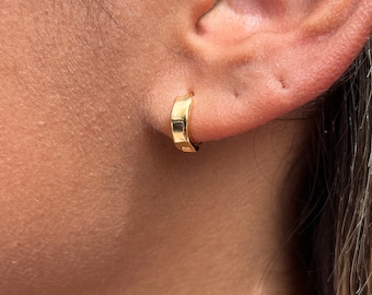 Puede incluir: Primer plano de una oreja con un pequeño aro de oro. El aro es simple y elegante, con un acabado liso y pulido.