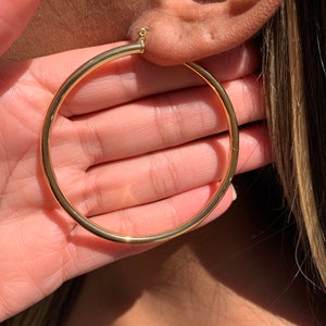 May include: Gold hoop earrings with a thick, round design. The earrings are large and have a simple, classic style.
