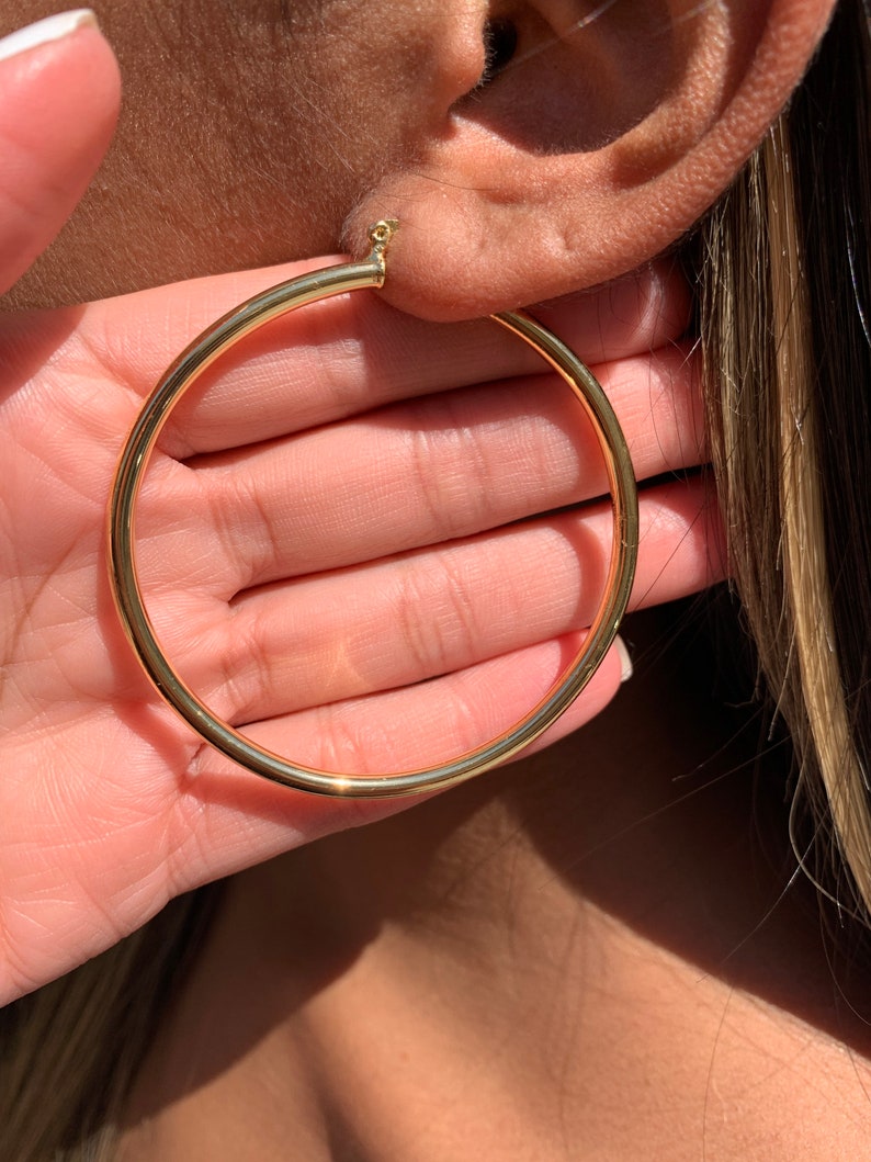 May include: Gold hoop earrings with a thick, round design. The earrings are large and have a simple, classic style.
