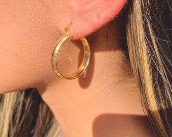 May include: Gold hoop earrings with a smooth, polished finish. The earrings are worn in a person's ear.