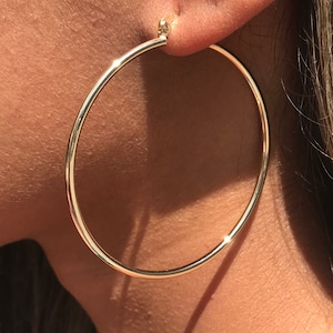 Op de afbeelding: Gouden creolen met een gladde, gepolijste afwerking. De oorbellen zijn groot en rond, met een diameter van ongeveer 5 cm.