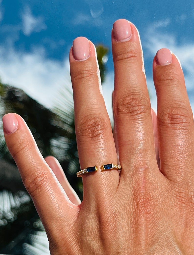 May include: A gold ring with two blue gemstones and small clear stones set in the band.