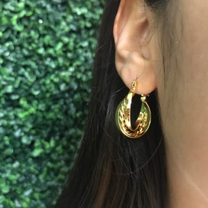 May include: A gold hoop earring featuring a dual-layered design with one smooth, polished band and one twisted, rope-textured band. The earring is circular in shape and has a reflective metallic finish, showcasing a classic interlocking style.