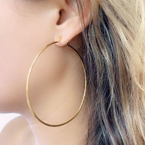 May include: Gold hoop earrings worn in a person's ear. The earrings are large and circular.
