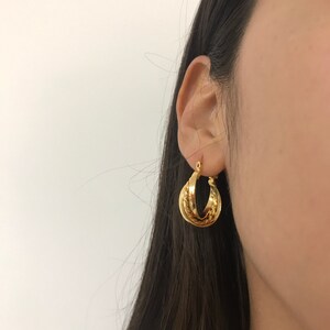 May include: A gold hoop earring featuring a double-layered design with one smooth, polished band and one twisted, rope-textured band. The earring is circular in shape and has a hinged closure mechanism visible at the top of the hoop structure.