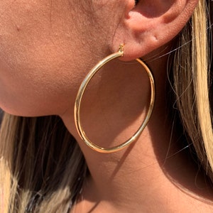 May include: Gold hoop earrings worn in a person's ear. The earrings are large and circular.