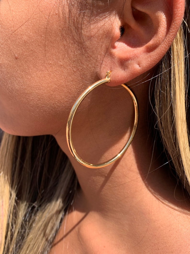 May include: Gold hoop earrings worn in a person's ear. The earrings are large and circular.