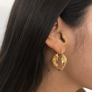 May include: A gold hoop earring featuring a twisted design with a polished finish. The earring consists of two interlocking bands, one with a smooth surface and the other with a textured, rope-like appearance, creating a layered look.
