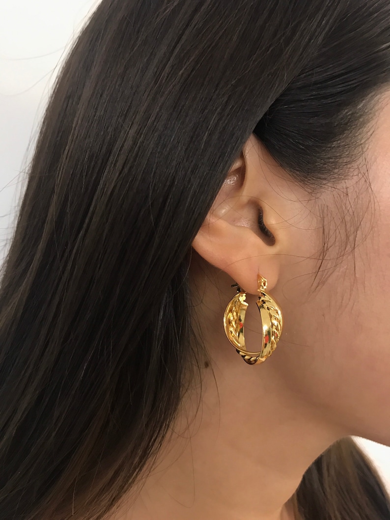 May include: A gold hoop earring featuring a twisted design with a polished finish. The earring consists of two interlocking bands, one with a smooth surface and the other with a textured, rope-like appearance, creating a layered look.