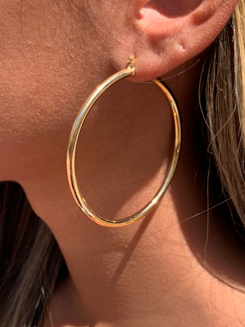 May include: A pair of large, gold hoop earrings. The earrings are simple and classic, with a smooth, polished finish.