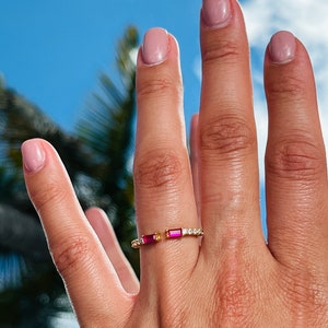 May include: A gold ring with two small red rectangular stones and a row of small clear stones.