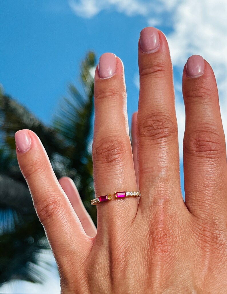 May include: A gold ring with two small red rectangular stones and a row of small clear stones.