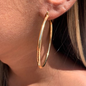 May include: Gold hoop earrings. The earrings are large and circular, with a smooth, polished finish.