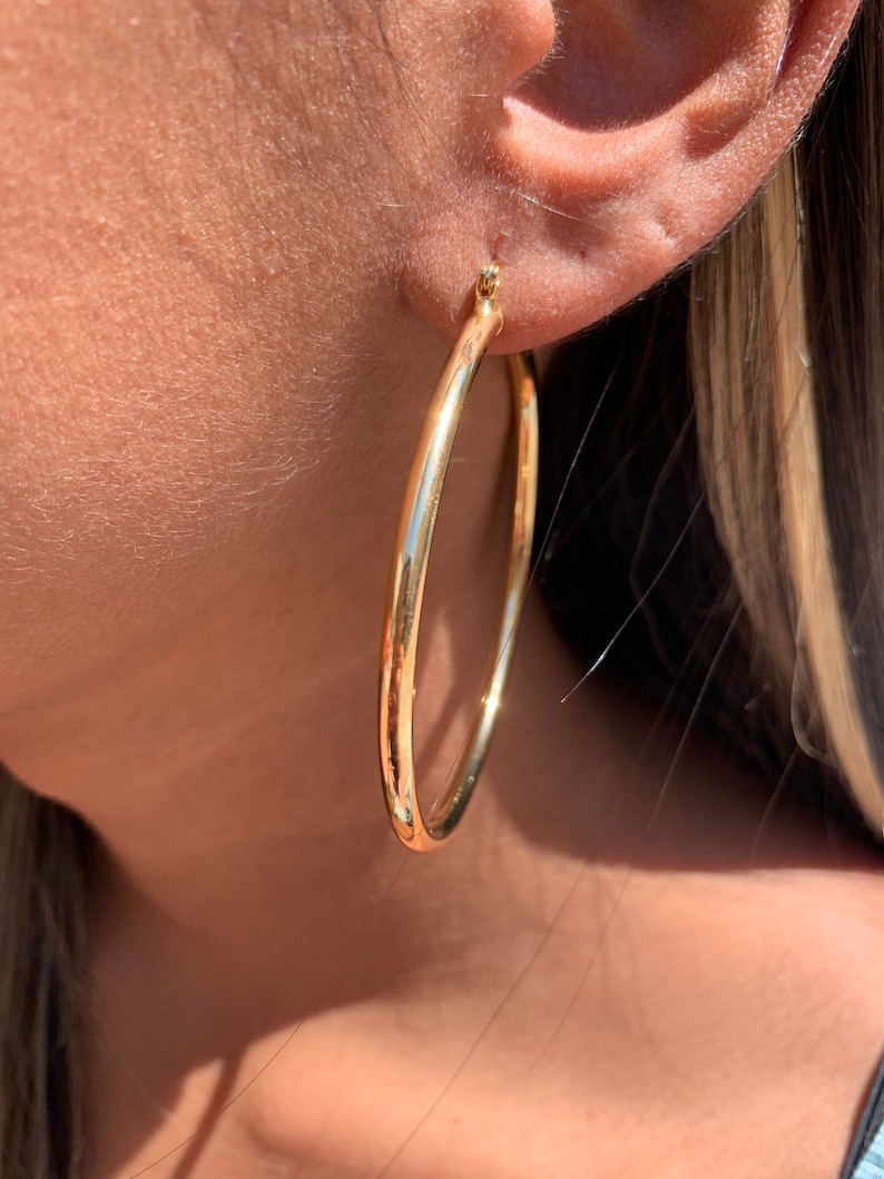 May include: Gold hoop earrings. The earrings are large and circular, with a smooth, polished finish.