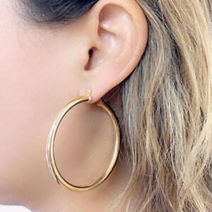 May include: Gold hoop earrings with a smooth finish. The earrings are large and have a classic design.