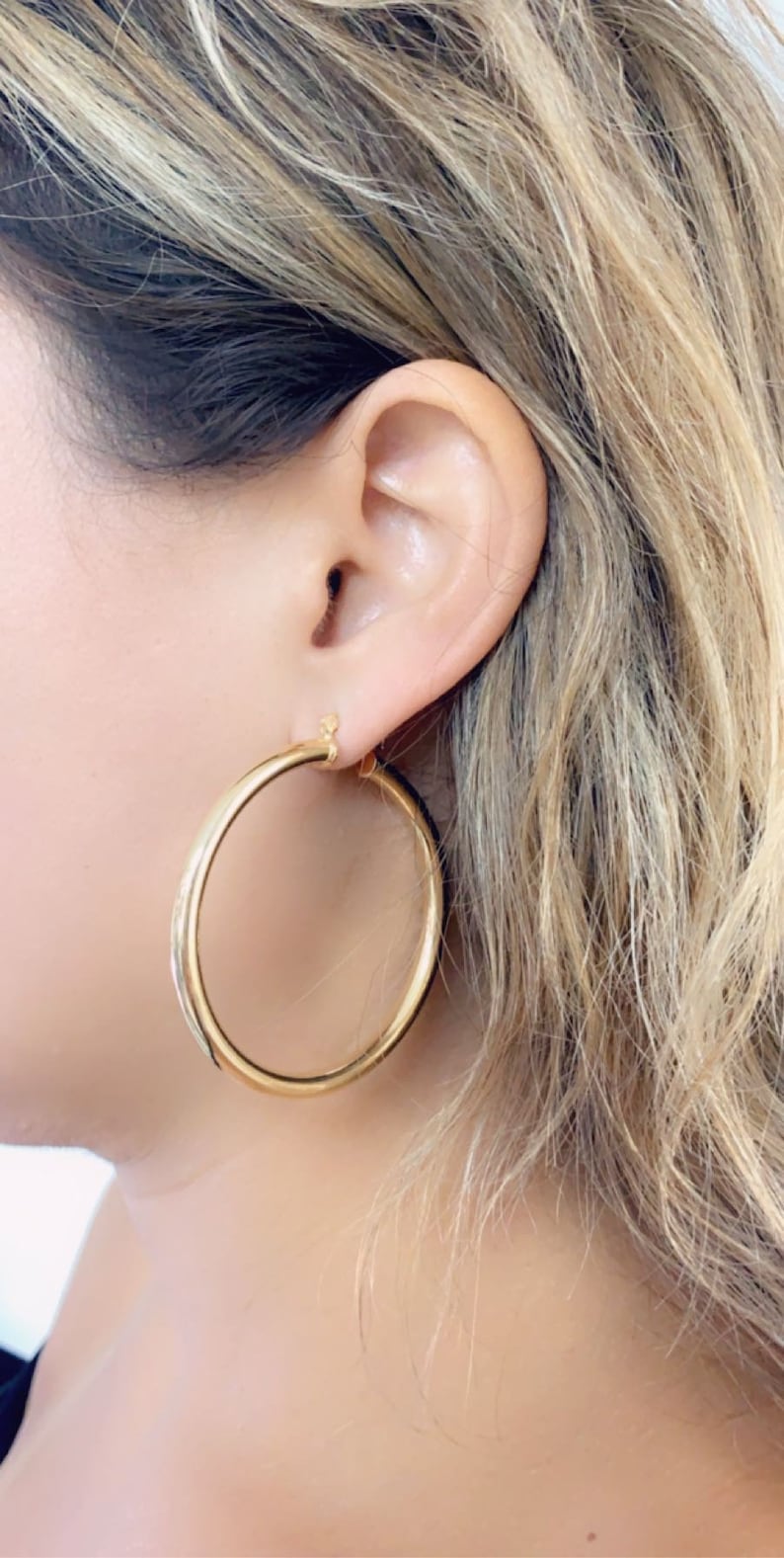 May include: Gold hoop earrings with a smooth finish. The earrings are large and have a classic design.
