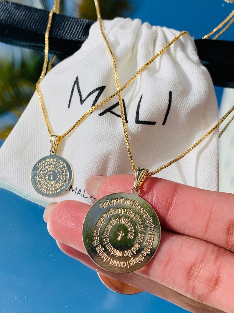 May include: Two gold necklaces with round pendants featuring a circular inscription. The inscription on the pendant in the foreground reads "God, grant me the serenity to accept the things I cannot change, the courage to change the things I can, and the wisdom to know the difference."