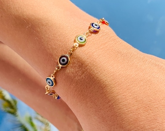 May include: A gold chain bracelet with multiple blue, green, red, and white evil eye charms. The bracelet is on a person's wrist.