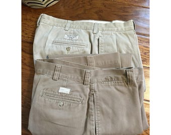 Peut inclure: Deux pantalons en coton de couleur kaki avec passants de ceinture, une poche arrière boutonnée et une étiquette blanche rectangulaire sur la poche. L'un porte une étiquette Ralph Lauren au-dessus de la poche, l'autre une étiquette blanche vierge.