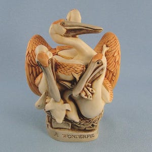 May include: A cream and tan colored sculpture depicting a group of pelicans in a nest. The birds have long beaks and textured wings. The base of the sculpture features the text A WONDERFUL, with the birds arranged in a cluster above the nest.