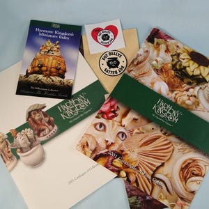 May include: A green and white brochure with the text "Harmony Kingdom" and "2001 Catalogue of Fine Gifts". The brochure features a variety of figurines, including a cat, a bird, and a sunflower.
