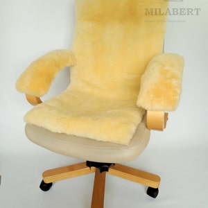 May include: A beige sheepskin office chair cushion with armrests. The cushion is made from natural sheepskin and is designed to provide comfort and support. The cushion is placed on a beige office chair with a wooden base and black wheels. The chair is on a white background. MILABERT Nature Style Inspiration.
