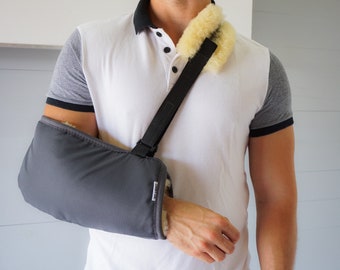 May include: A gray padded arm sling with a black adjustable strap. The strap is worn over the shoulder and has a soft, light brown fleece lining.